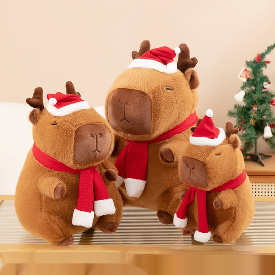 Three festive capybaras sitting on a table. Christmas Plushie, Capybara Plushie, Squishmallow.